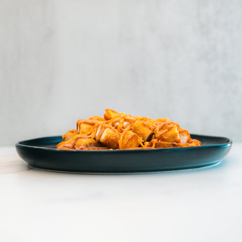 A dark plate holds a serving of "Closed on Sunday" Crispy Chicken Bowl with golden, crispy pieces drizzled in syrup—an inviting, macro-friendly lunch—set on a white surface against a light gray background.
