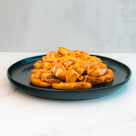 The "Closed on Sunday" Crispy Chicken Bowl features crispy waffle fries topped with melted cheese, making it a macro-friendly lunch. Served on a black plate over white marble, set against a light gray background.