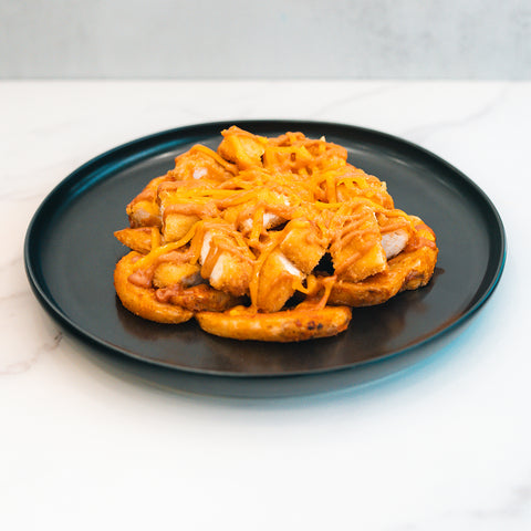 The "Closed on Sunday" Crispy Chicken Bowl features crispy curly fries topped with melted cheddar cheese, served on a black plate over a white marble surface—ideal for a macro-friendly lunch.