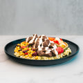 The Texas Queso Steak Bowl features grilled beef pieces, rice, mixed vegetables, and a drizzle of white sauce atop a black plate on a light marble surface—delivering a deliciously satisfying, high-protein, gluten-free meal.