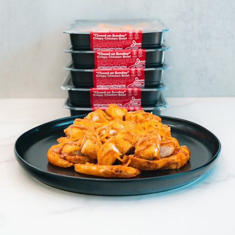 A cheesy, golden-brown pull-apart bread is in front, with four stacked "Closed on Sunday" Crispy Chicken Bowl packages visible in the background.