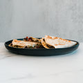 Three folded Philly Cheesesteak Quesadillas with grilled tortillas and visible fillings sit on a dark plate against a light marble surface and a gray background—ideal for high-protein, macro-friendly meal prep.