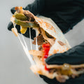 A gloved hand holds the Philly Cheesesteak Quesadilla, packed with tender beef, green peppers, onions, red peppers, and melted cheese stretching as it’s pulled apart—making it a delicious and macro-friendly option ideal for high-protein meal prep.