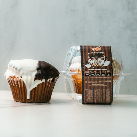 Two Buffin Muffin - Black White Cookie treats—one unwrapped, one in a clear box with a “Black White Cookie” label—feature split white and chocolate icing. A light background highlights these protein-packed muffins.