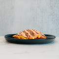 A black plate holds a slice of bread topped with a creamy spread, ground meat, and visible slices of pickles and cheese—reminiscent of the Animal Style West Coast Beef Bowl. This high-protein meal prep option stands out against the light gray background, set on a pristine white marble surface.