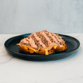 A serving of the Animal Style West Coast Beef Bowl features ground meat, melted cheese, diced onions, and a creamy sauce atop a waffle on a black plate—an ideal choice for anyone craving a macro-friendly take on this West Coast favorite.