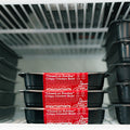 Three black plastic "Closed on Sunday" Crispy Chicken Bowl containers, a high-protein meal, are stacked in a freezer. Frost lines are visible on the shelf above, with more containers to the right.