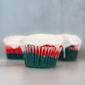 Three Red, White Blue Buffin Muffins—with green, red, and white layers in striped wrappers and topped with white icing—make a festive patriotic protein treat on a light surface against a soft grey background.