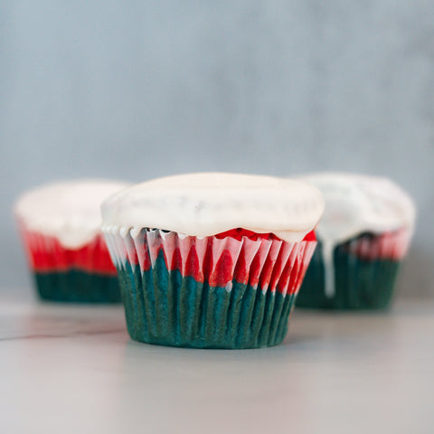 Three Red, White Blue Buffin Muffins—with green, red, and white layers in striped wrappers and topped with white icing—make a festive patriotic protein treat on a light surface against a soft grey background.