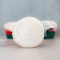 A Red, White Blue Buffin Muffin, topped with smooth white icing, sits in front of two frosted high-protein muffins in green and red wrappers on a light surface against a pale gray background.
