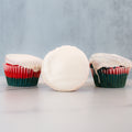 Three Red, White Blue Buffin Muffins with red and green wrappers and smooth white frosting are displayed—two upright, one on its side—on a light gray and white surface, perfect for a festive 4th of July treat.