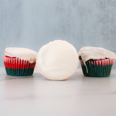 Three Red, White Blue Buffin Muffins with red and green wrappers and smooth white frosting are displayed—two upright, one on its side—on a light gray and white surface, perfect for a festive 4th of July treat.