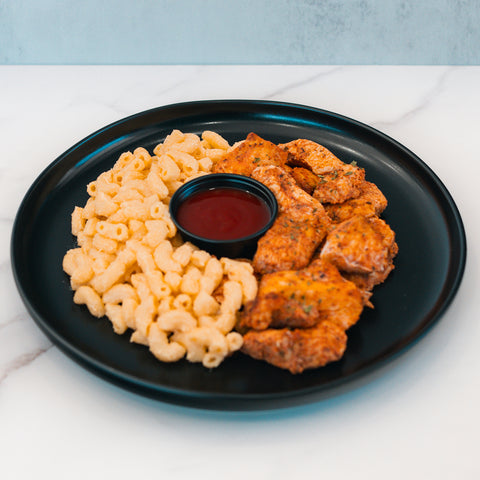 Buffalo Mac N Chicken features creamy Buffalo mac, seasoned chicken pieces, and a side of red dipping sauce on a black plate—perfect as a macro-friendly comfort food.