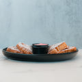Three slices of Strawberry Protein French Toast, dusted with powdered sugar, are arranged on a black plate with a small cup of syrup in the center. The setting is minimal, with a light background and a marble surface—perfect for those seeking a low sugar breakfast without sacrificing indulgence.