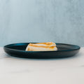 Two pieces of grilled halloumi cheese on a dark plate rest on a light marble surface with a pale blue background—ideal for meal prep or pairing with Competition Approved Oven Baked Cod 1lb for a protein-rich, balanced meal.