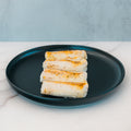 Three pieces of Competition Approved Oven Baked Cod 1lb are neatly arranged in a row on a black plate atop white marble—a delicious, high-protein option for meal prep.