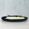 The Arnold 2022 Bowl features white rice, asparagus, grilled chicken, and a side of sauce in a black plate—perfect for a healthy lunch, presented on a white surface with a light gray background.