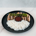 The Arnold 2022 Bowl features sliced grilled chicken, white rice, grilled asparagus, and a dark dipping sauce in a sleek black plate—ideal for a healthy lunch or easy chicken and rice meal prep.