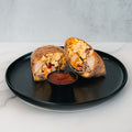 The Breakfast Burrito, filled with scrambled eggs, turkey bacon, and vegetables, is cut in half and served on a black plate with a small container of red sauce in the center.