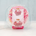 A packaged Strawberry Crunch Milkshake - Exclusive- 20 ice cream cake from Buffin Bakery, adorned with pink, red, and white crunchy toppings, is displayed on a light surface against a pale background—a delightful treat reminiscent of early-access products.