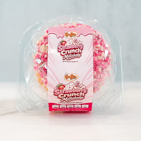 A packaged Strawberry Crunch Milkshake - Exclusive- 20 ice cream cake from Buffin Bakery, adorned with pink, red, and white crunchy toppings, is displayed on a light surface against a pale background—a delightful treat reminiscent of early-access products.
