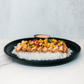 The Southwest Chicken Bowl features white rice, sliced grilled chicken, corn, diced tomatoes, and herbs—a gluten-free dish served with creamy sauce on the side.