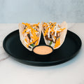 Baja Chicken Tacos feature grilled chicken, shredded cheese, and greens in low-carb flour tortillas, served with a creamy orange dipping sauce on a black plate—an ideal high-protein meal prep option.