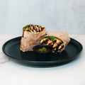 The Grilled Chicken Pesto Wrap, packed with protein and fresh greens, is cut in half and served with a side of green sauce—an ideal meal prep option for busy days.