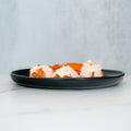 A black plate features Buffalo Chicken Meatballs—three breaded bites topped with a creamy sauce—served alongside a small portion of orange chips on a white marble surface with a light gray background, making them perfect for a healthy dinner or your next meal prep.