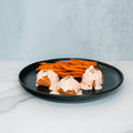 Buffalo Chicken Meatballs are served on a black plate and garnished with fresh herbs, accompanied by crispy sweet potato fries for a healthy dinner. Set against a white marble surface with a light gray background, they’re the perfect choice for easy meal prep.