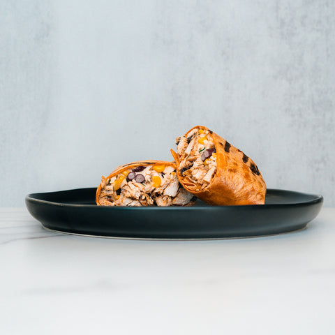 A Broritto Burrito, sliced in half on a black plate, reveals its high-protein fillings of shredded meat, black beans, rice, and cheese against a light background.