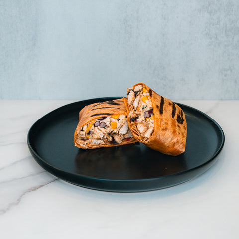 A Broritto Burrito, grilled and cut in half to reveal its filling of chicken, corn, black beans, and vegetables, sits on a black plate atop a white marble surface.