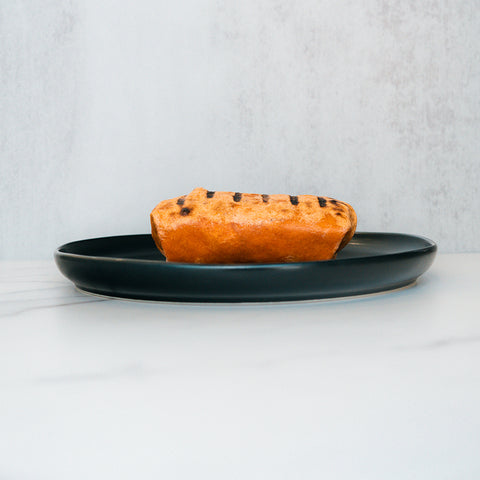 A Broritto Burrito with distinct grill marks sits on a dark plate, placed on a light-colored surface with a pale, textured background—reminiscent of a fiber-rich, high-protein wrap freshly pressed and ready to enjoy.