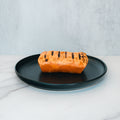 A Broritto Burrito, golden-brown and rectangular with distinct dark grill marks, sits on a black plate against a light marble surface and gray background.
