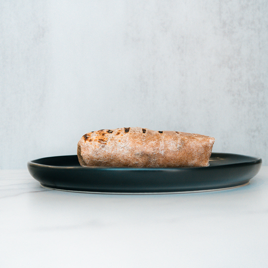 A single The Arches Mac Daddy Wrap sits on a dark plate against a light background, perfect for crafting a macro-friendly lunch or assembling a high-protein meal prep wrap.