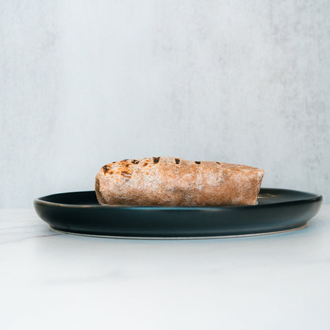 A single The Arches Mac Daddy Wrap sits on a dark plate against a light background, perfect for crafting a macro-friendly lunch or assembling a high-protein meal prep wrap.
