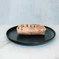 The Arches Mac Daddy Wrap, a high-protein meal prep option inspired by cheeseburger flavors, features grilled char marks and is served on a black plate with a light marble surface and pale blue background—perfect for a macro-friendly lunch.