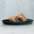 Two pieces of the Grilled Chicken Parmesan Wrap are placed on a dark round plate, set against a light grey background on a white marble surface.