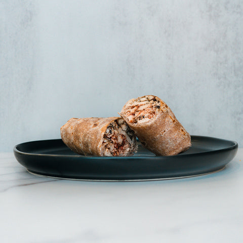 Two pieces of the Grilled Chicken Parmesan Wrap are placed on a dark round plate, set against a light grey background on a white marble surface.