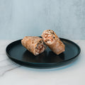 A Grilled Chicken Parmesan Wrap, sliced in half and filled with tender shredded chicken and vegetables, rests on a black plate against a light marble background—an ideal option for healthy meal prep.