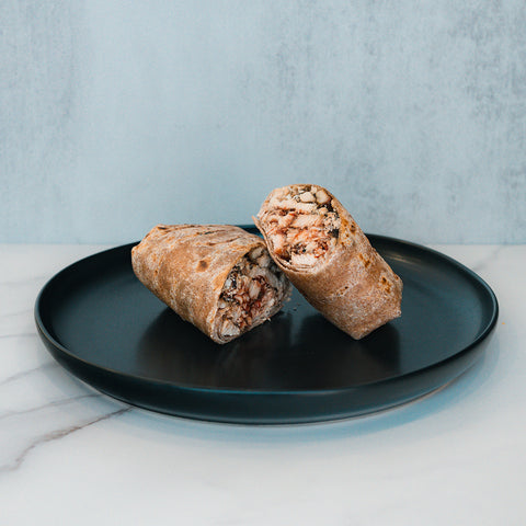 A Grilled Chicken Parmesan Wrap, sliced in half and filled with tender shredded chicken and vegetables, rests on a black plate against a light marble background—an ideal option for healthy meal prep.