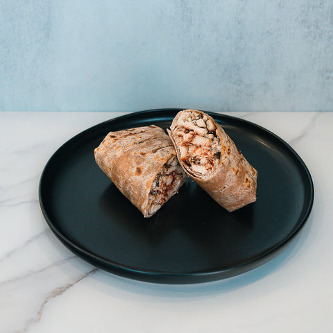 A Grilled Chicken Parmesan Wrap, sliced in half, is served on a black plate. Made with a whole wheat tortilla and filled with shredded chicken and vegetables, the Grilled Chicken Parmesan Wrap sits atop a white marble surface against a light blue background—an ideal choice for healthy meal prep.