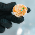A hand in a black glove holds a bitten Protein Buff Pops - Dunk’d Out, featuring a white coating and colorful sprinkles inside, against a blurred light background—an indulgent yet low calorie protein snack.
