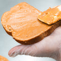 A gloved hand spreads creamy Peanut Butter Jelly Sandwich filling onto bread—a delicious, high-protein option perfect for your post-workout snack.