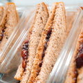 Close-up of several Peanut Butter Jelly Sandwiches made with whole wheat bread, arranged upright in clear plastic containers, showing the protein-packed filling between the slices.
