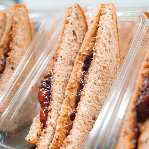 Close-up of several Peanut Butter Jelly Sandwiches made with whole wheat bread, arranged upright in clear plastic containers, showing the protein-packed filling between the slices.