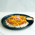 A black plate with white rice topped with seasoned ground meat, shredded cheddar cheese, diced red onions, and sliced jalapeños. A small black cup of creamy dipping sauce is on the side.