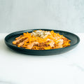A black plate holds a serving of food with ground beef, shredded cheddar cheese, chopped onions, and a drizzle of creamy orange sauce on top, set against a white background.