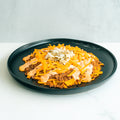 A black plate with a serving of taco salad topped with shredded cheddar cheese, ground beef, chopped onions, and a creamy orange sauce, on a white surface with a light gray background.