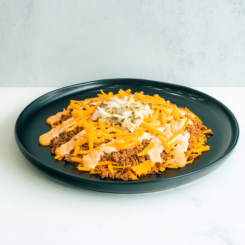 A black plate with a serving of taco salad topped with shredded cheddar cheese, ground beef, chopped onions, and a creamy orange sauce, on a white surface with a light gray background.
